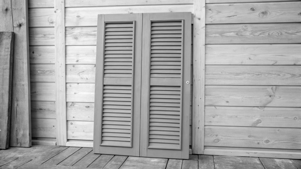 Muted sage green shutters rest against a natural wood wall the subtle tones complementing one another and evoking a sense of earthy tranquility.
